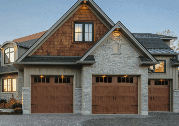 Three beautiful wood looking garage doors on a stone home with a peaked roof