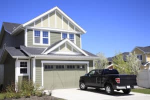 A lovely sage coloured home with detailed and modern garage doors and a black truck in the driveway
