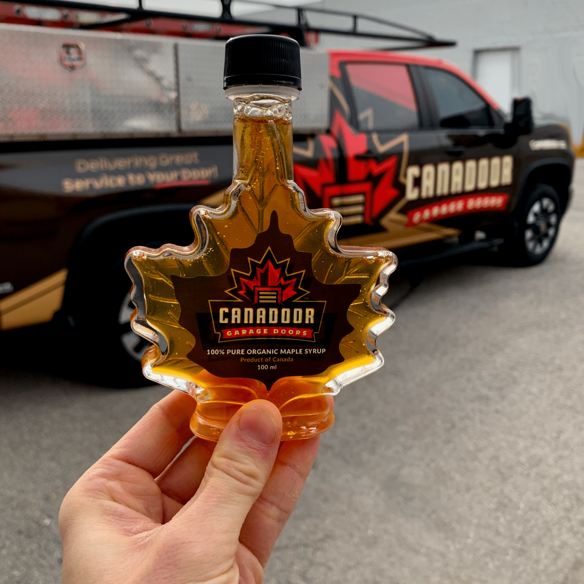 Bottle of maple syrup with a garage door technician service vehicle behind it