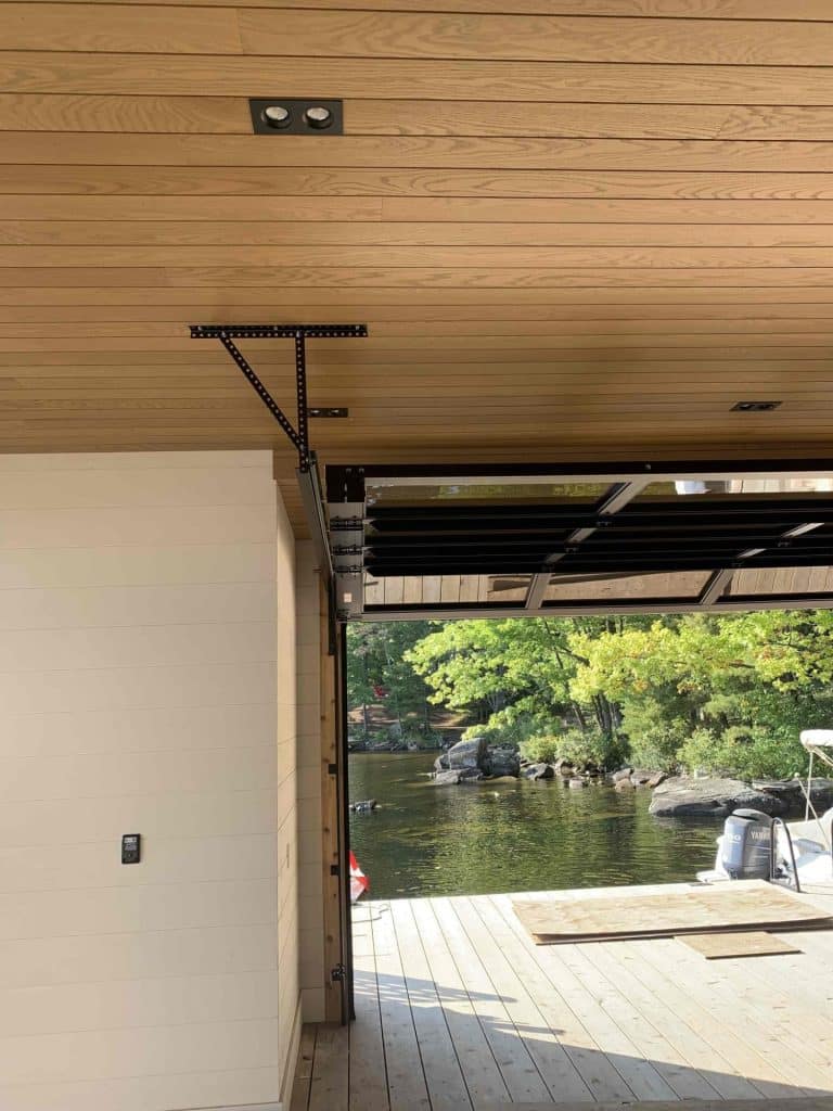 Black full-view glass garage door opening onto a lakeside dock