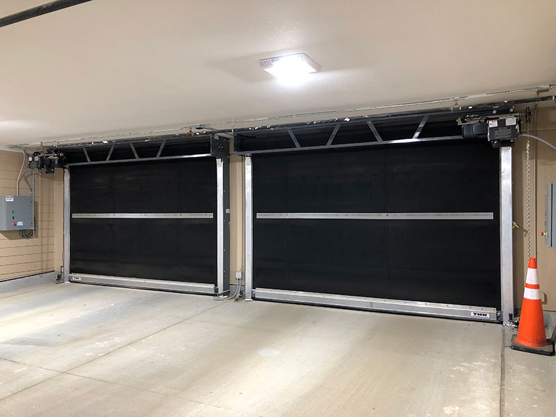 Two black commercial garage doors with overhead door operators in a parking garage