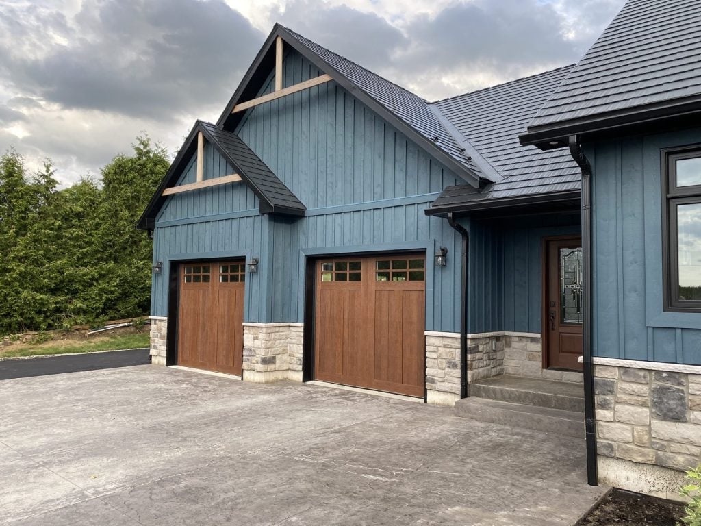 Two wood-look garage doors with decorative windows on a blue residential home