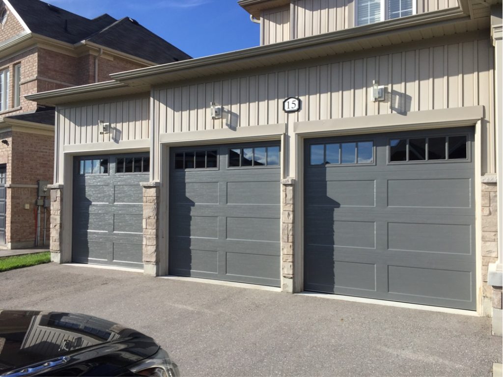 Three gray sectional garage doors with rectangular windows on a residential building