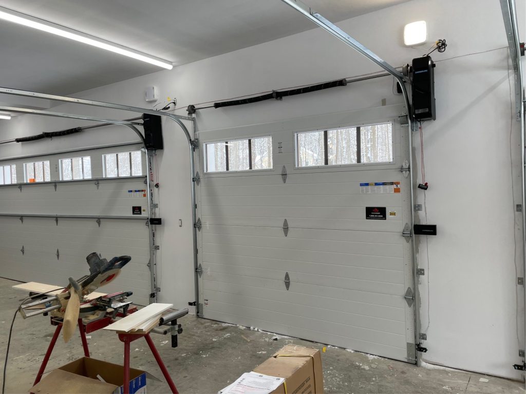 Two white sectional garage doors with windows and wall-mounted openers