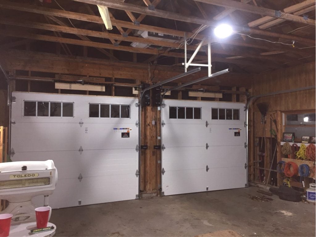 Two white sectional garage doors with overhead door tracks and openers