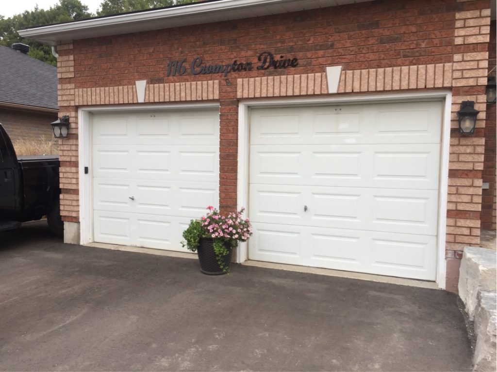 Two white raised-panel garage doors on a brick residential garage